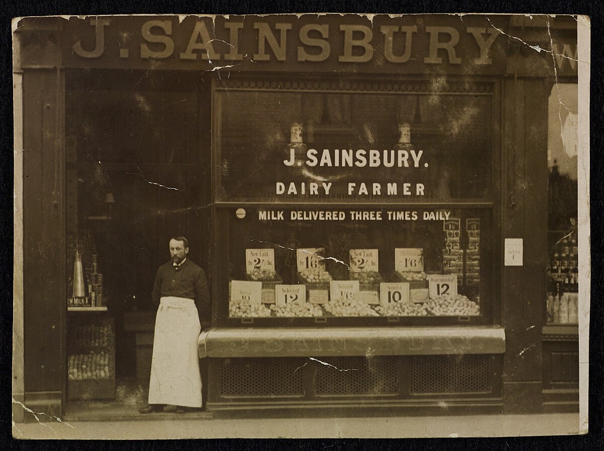 Historic Image from the Sainsbury archive, Showcasing 150 years of retail history. Men in white aprons standing out front of Sainsbury licenced shop and vehicles.
